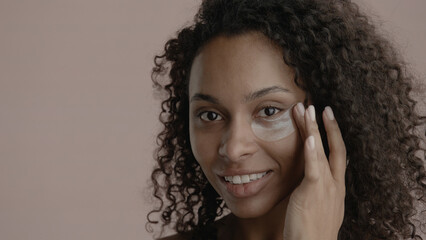 CU Portrait of attractive African-American female doing her skincare routine. Applying eye patches....