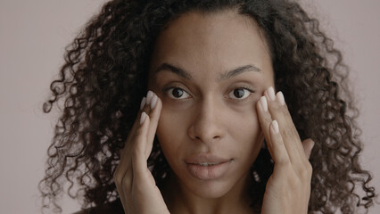 CU Portrait of attractive African-American female doing her skincare routine. Studio shot, soft...