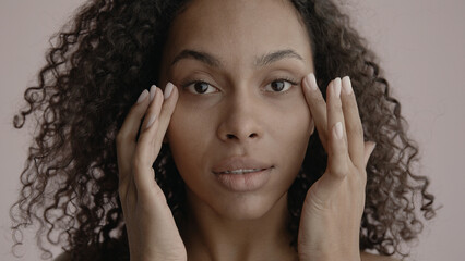 CU Portrait of attractive African-American female doing her skincare routine. Studio shot, soft...