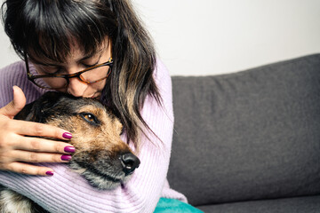 Adorable shot of Hispanic young woman kissing ang hugging her dog at home. Copy space on the right side for text