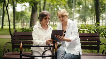 Adult daughter teaching senior mother how to use a tablet while sitting in park