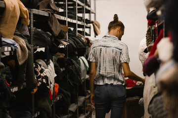 Madrid, Spain. September 1, 2022 Young woman walks among rows of shelves of shabby clothes. A girl...