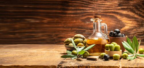 Obraz na płótnie Canvas Glass container with olive oil branches and olives on a wooden background. Long banner format