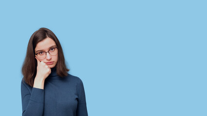 Portrait of a frustrated, tired, pensive student girl in glasses and a sweater holding her hand to her face