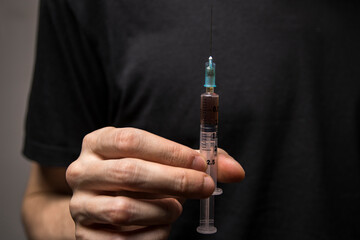 Close-up of a hand holding a heroin syringe. Drug addiction concept