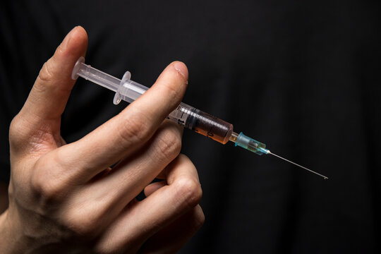 Close-up of a hand holding a heroin syringe. Drug addiction concept