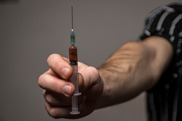 Close-up of a hand holding a heroin syringe. Drug addiction concept - obrazy, fototapety, plakaty