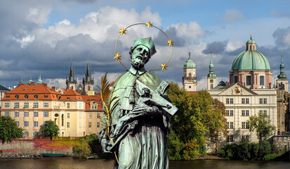 Statue of Saint John Nepomuk with Crucifix of Jesus Christ on background of city landscape of...