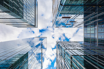 Look up to high skyscrapers corporate buildings with glass walls and reflecting beautiful cloudy...