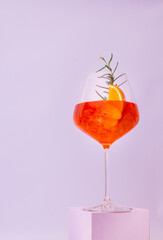 A glass with an alcoholic cocktail on a podium, an Aperol with dry wine and ice and a slice of orange and rosemary close-up in delicate pastel colors