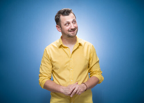 Happy bearded man looking up to side. Waist-up smile expression of guy looks to side over blue background, dresses in yellow shirt