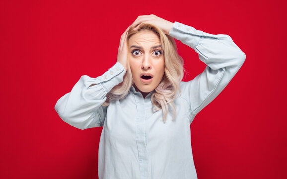 Astonished woman with hands on his head, isolated on red background. Shocked girl