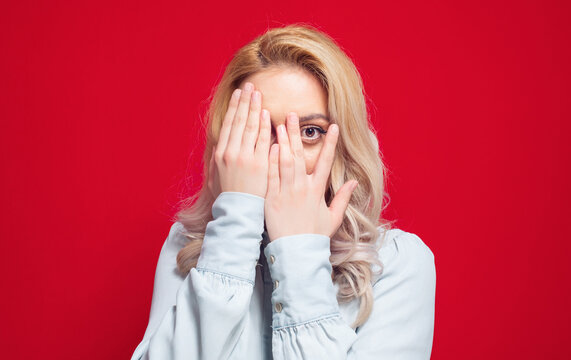 Peaking. Obscured face. Close up young woman covering face with hands. Shame, isolated on red background. Ashamed girl