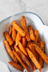 Sweet potato French fries chips in a white enamel dish bowl. On a marble background