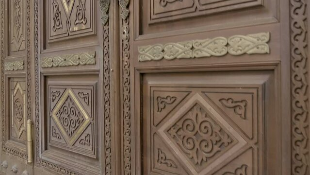 Large wooden entrance door to the mosque, decorated with beautiful patterns and Arabic script, beautifully carved wood and brass handles. Shot in motion