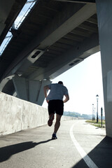 rear view of a jogger running under a bridge