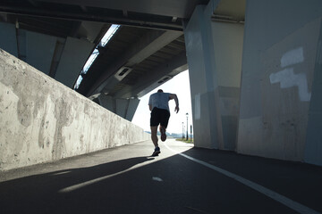 Fototapeta na wymiar Rear view of a running sportsman under a bridge