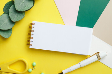 School supplies concept. Photo of white and yellow stationery, pen, scissors and paper notebook on a yellow background