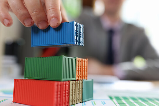 Business man arranging stack of freight cargo containers on office desk with financial documents.