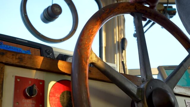 Hand turns big old wooden steering wheel on boat. Inside navigational bridge.