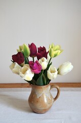 Bouquet of white and pink tulips in a small stoneware pot placed on a wooden console with an ecru table runner.