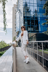 Beautiful business woman in white suit and sunglasses during break standing near modern office building