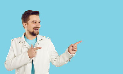 Cheerful man recommend good offer or promotion deal pointing to empty space on bright light blue background. Caucasian man in white jacket is looking at place he is pointing to with both hands. Banner