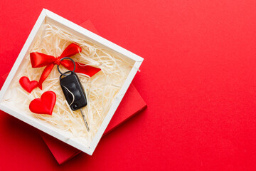 Black car key in a present box with a ribbon and red heart on colored background. Valentine day composition Top view - obrazy, fototapety, plakaty