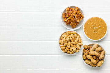 Sweet peanut brittle, peanuts and peanuts butter on white table. Top view.