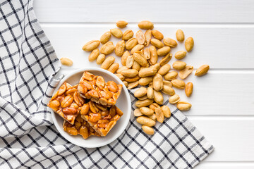 Sweet peanut brittle. Tasty peanuts in caramel on checkered napkin. Top view. - obrazy, fototapety, plakaty