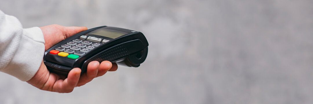 Payment terminal for cashless payments in hand. Paying with a credit card. Long banner.