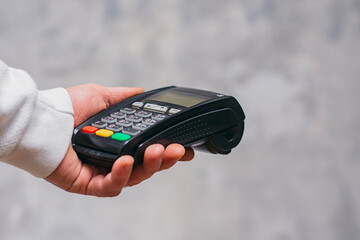 Man holds a payment terminal for cashless payments in his hand, against the background of a...
