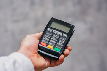 Man holds a payment terminal for cashless payments in his hand, against the background of a concrete wall.