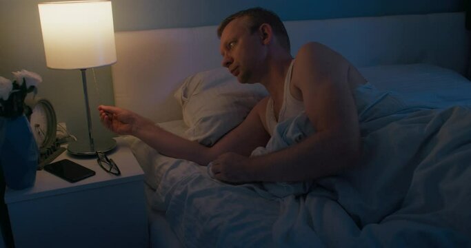 Man goes to sleep take off eyeglasses swithig off light on nightstand, medium shot