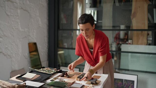 Serious brunette woman architect puts colour samples on a table in the office