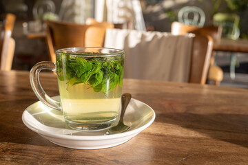 Fresh mint tea in a glass transparent mug with spoon on a wooden table in a restaurant