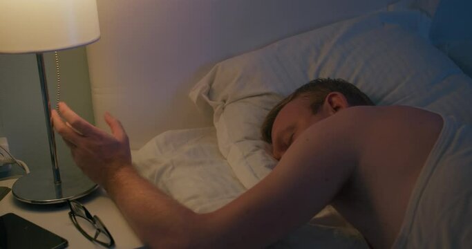 Man goes to sleep at night, swithig off light on nightstand, medium close-up shot
