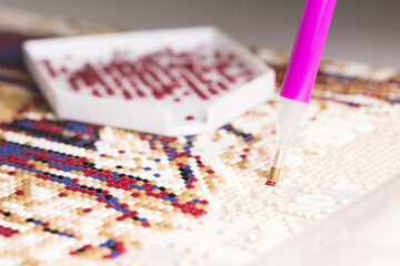 The moment of gluing a red rhinestone with a stylus onto a diamond mosaic painting. The process of creating a picture of rhinestones