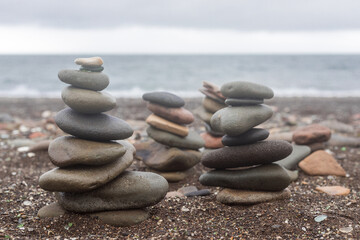 Fototapeta na wymiar Pyramid stones balance on the sand of the beach. The object is in focus, the background is blurred. Zen Tower made of stones.Many pyramids of stones on the beach.