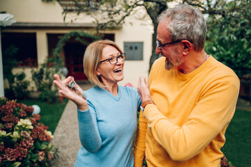 Senior couple holding keys and standing outside their new home