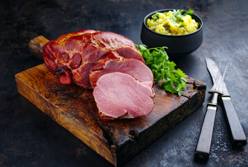 Traditionell geschmortes badisches Schäufele mit Kartoffelsalat und Petersilie aufgeschnitten als Draufsicht auf einem rustikalen Holz Schneidebrett 