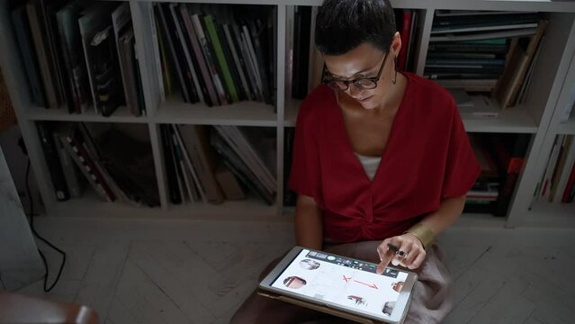 Confident brunette woman architect in eyeglasses working on tablet while sitting on the floor in the office