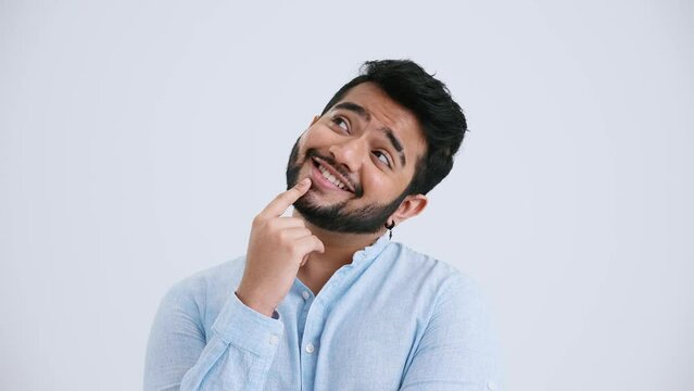 Pensive Indian man with piercing wearing blue shirt thinking about something in the grey studio