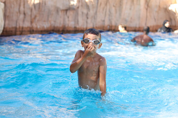 Young boy kid child six years old splashing in swimming pool having fun leisure activity wearing...