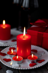 Saint Valentine's Day celebration. Red burning candles, hearts, gift box, postcard on dark wooden background. Happy holiday . Table decor for festive dinner, romantic atmosphere