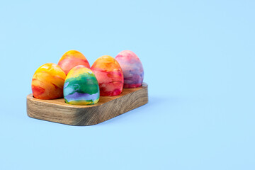 Colorful Easter eggs in a wooden egg stand on a blue background with a place for text. Happy Easter concept. Greeting card.