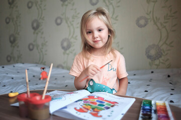 A four-year-old girl is engaged in drawing with multi-colored paints.