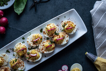 Deviled eggs garnished with smoked paprika , sliced radish , and chopped basil.