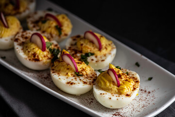 Deviled eggs garnished with smoked paprika , sliced radish , and chopped basil.