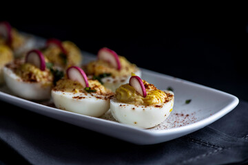 Deviled eggs garnished with smoked paprika , sliced radish , and chopped basil.